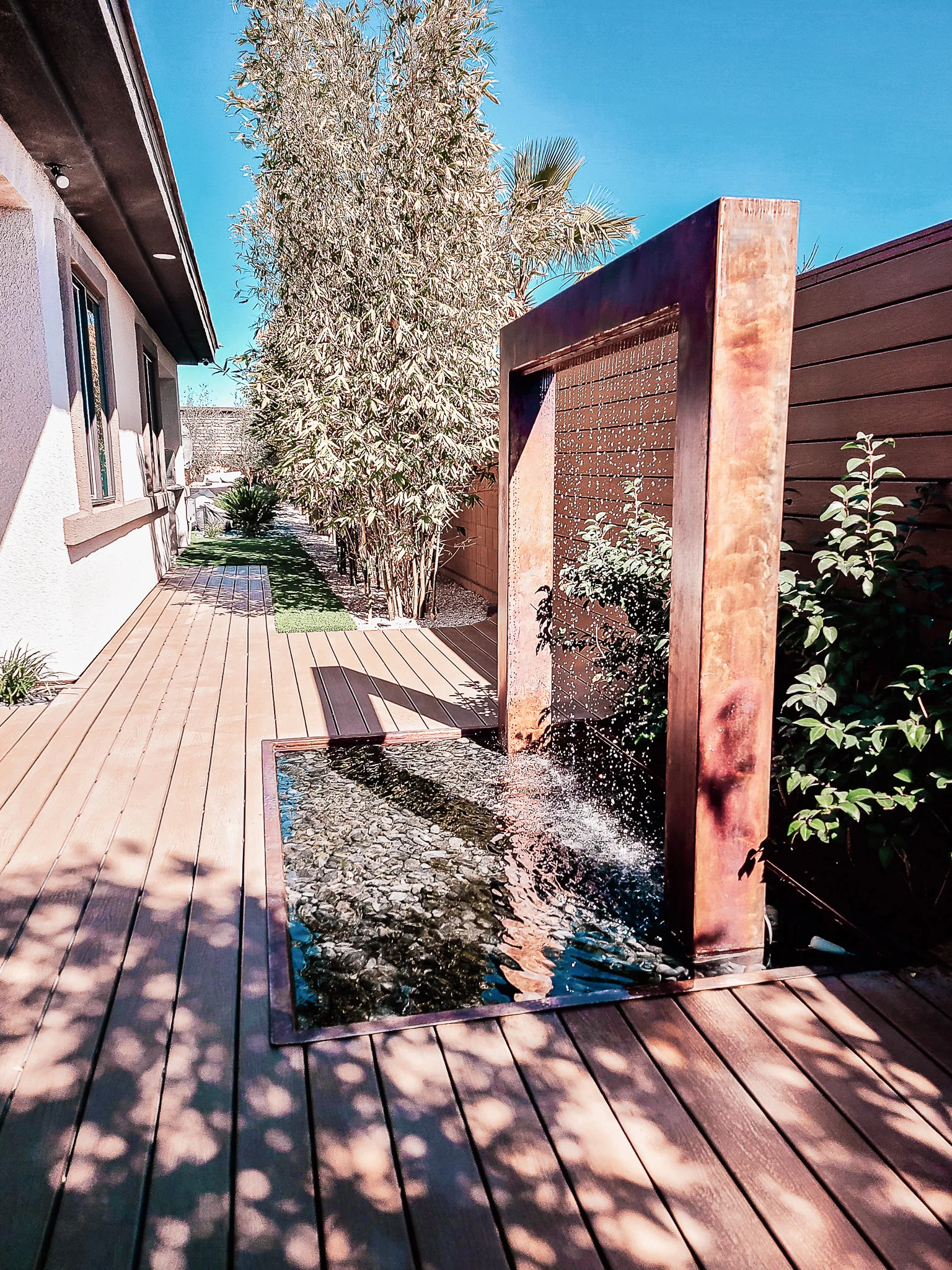 Rusted steel water curtain feature on composite deck with desert landscaping and tall ornamental grasses