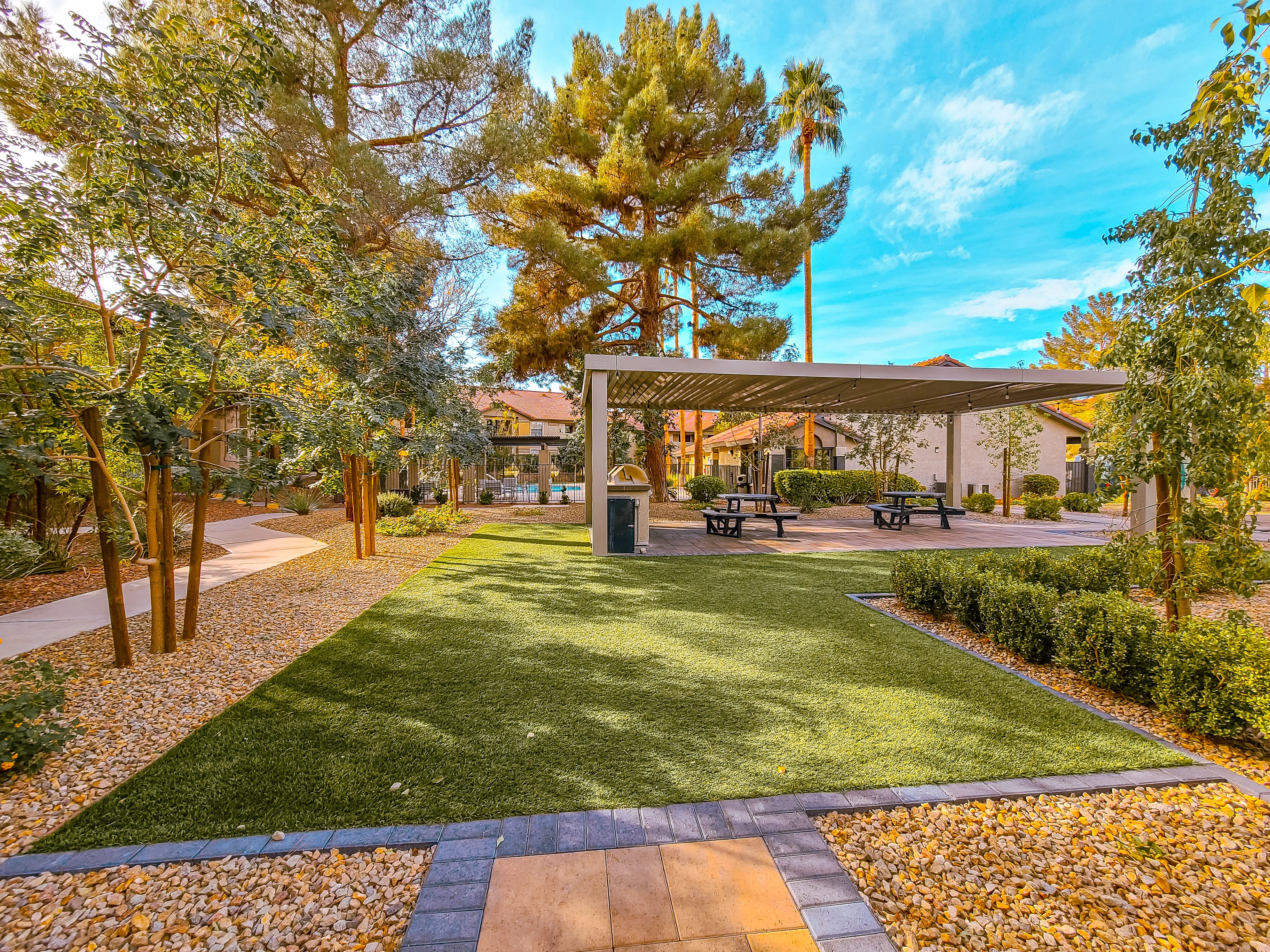 Modern patio cover with picnic tables, synthetic turf, and desert landscaping in apartment complex courtyard