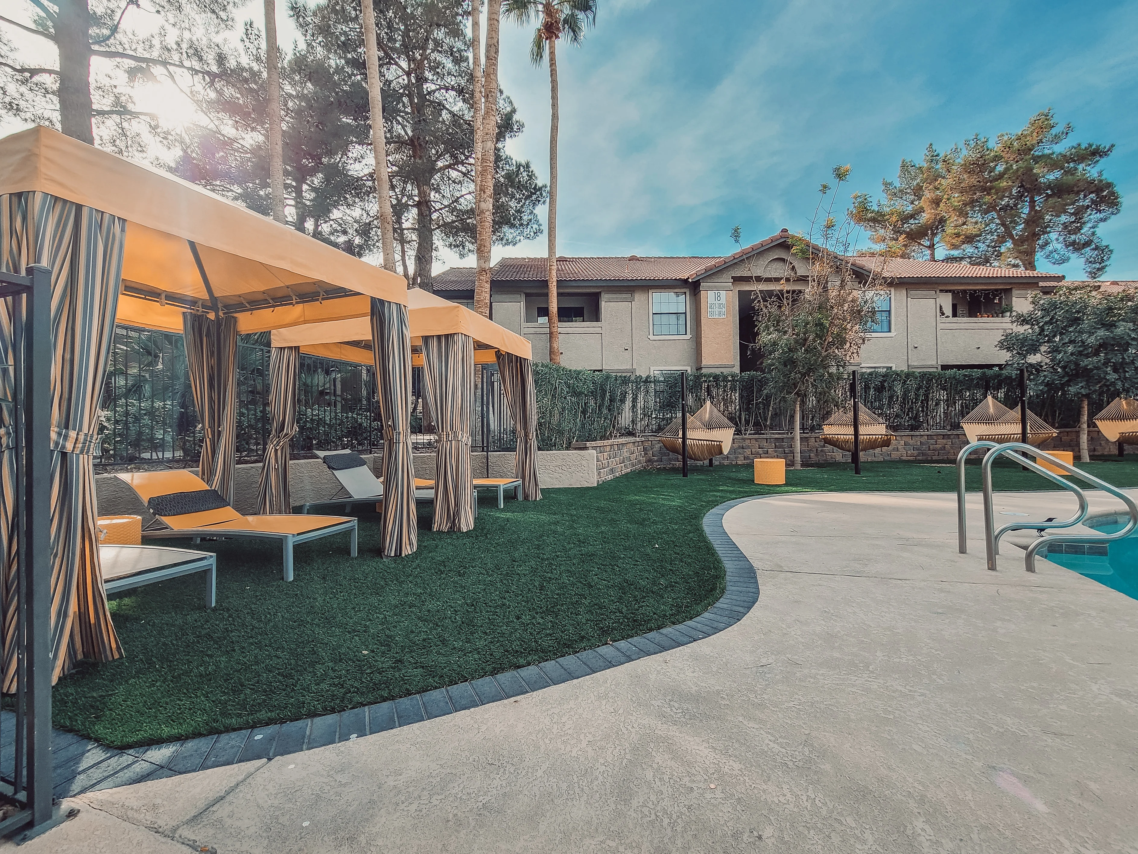 Poolside cabanas with orange canopies, synthetic turf, and curved concrete patio