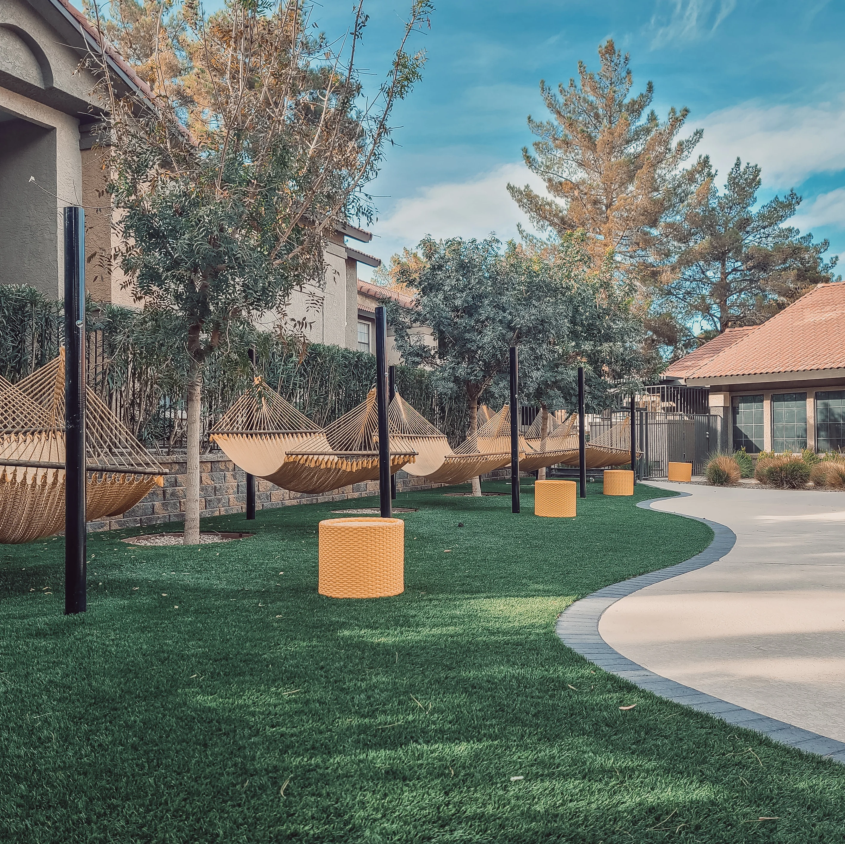 Modern backyard with tan hammocks, black posts, synthetic grass, and curved concrete pathways