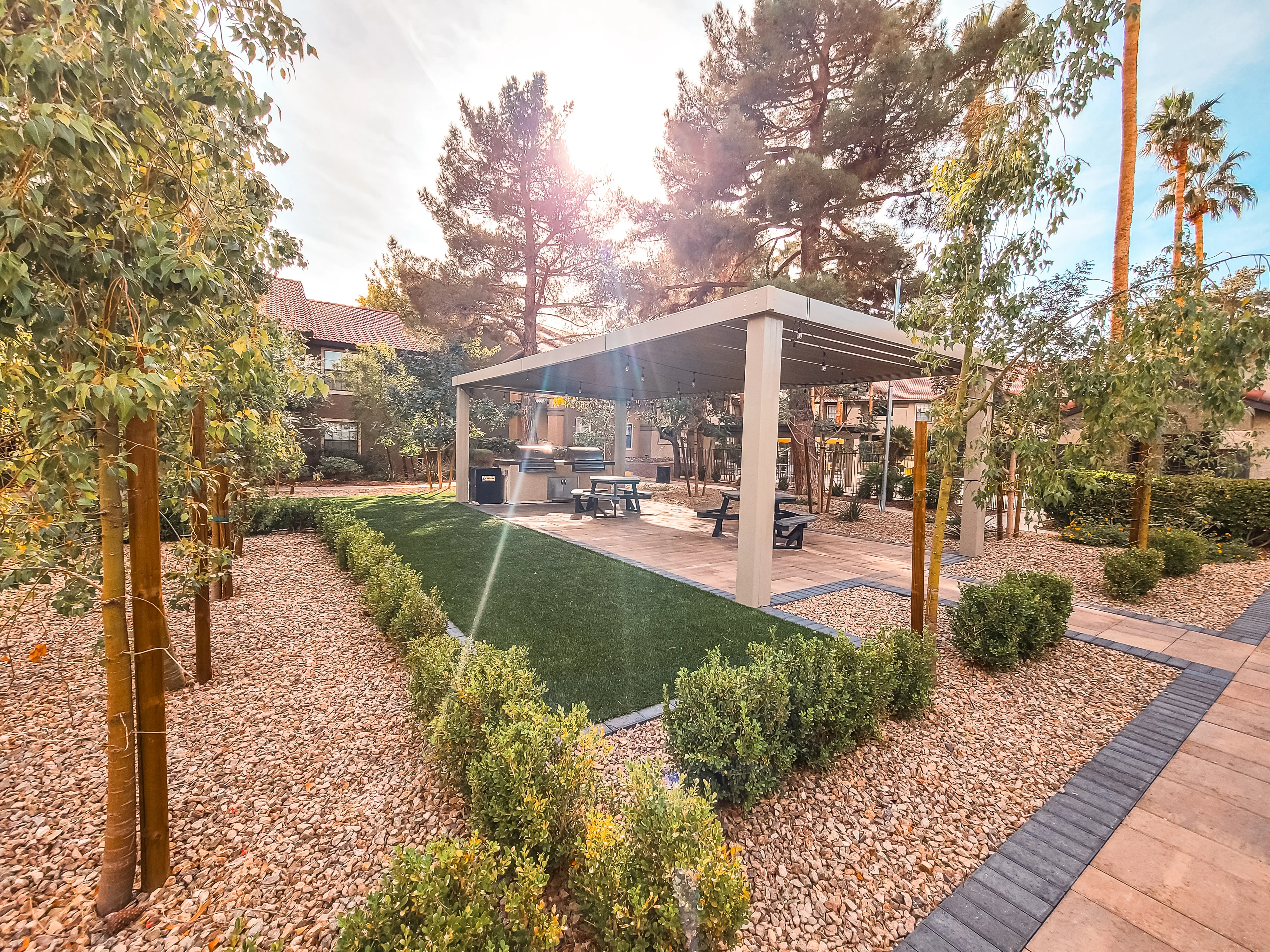 Modern white patio cover with columns over decorative gravel, lawn, and landscaped shrubs