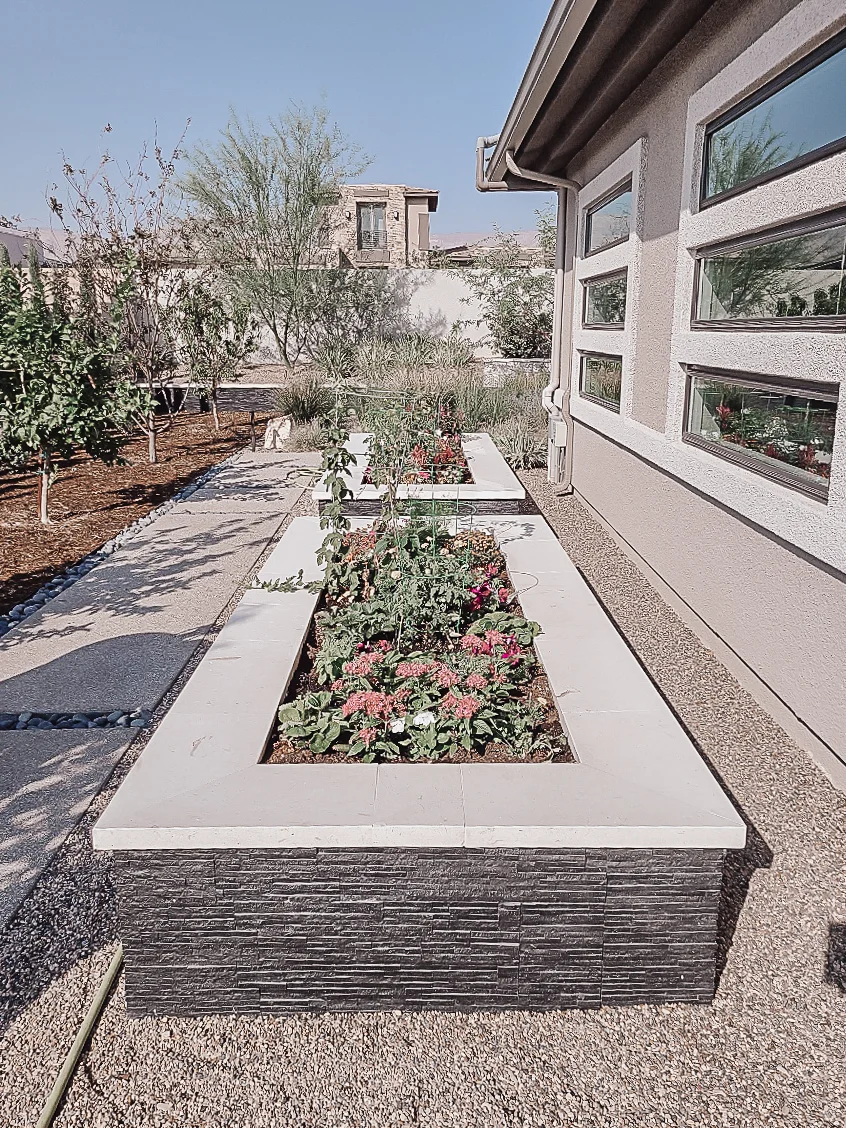 Raised garden bed with stone veneer and flowering plants along modern home exterior