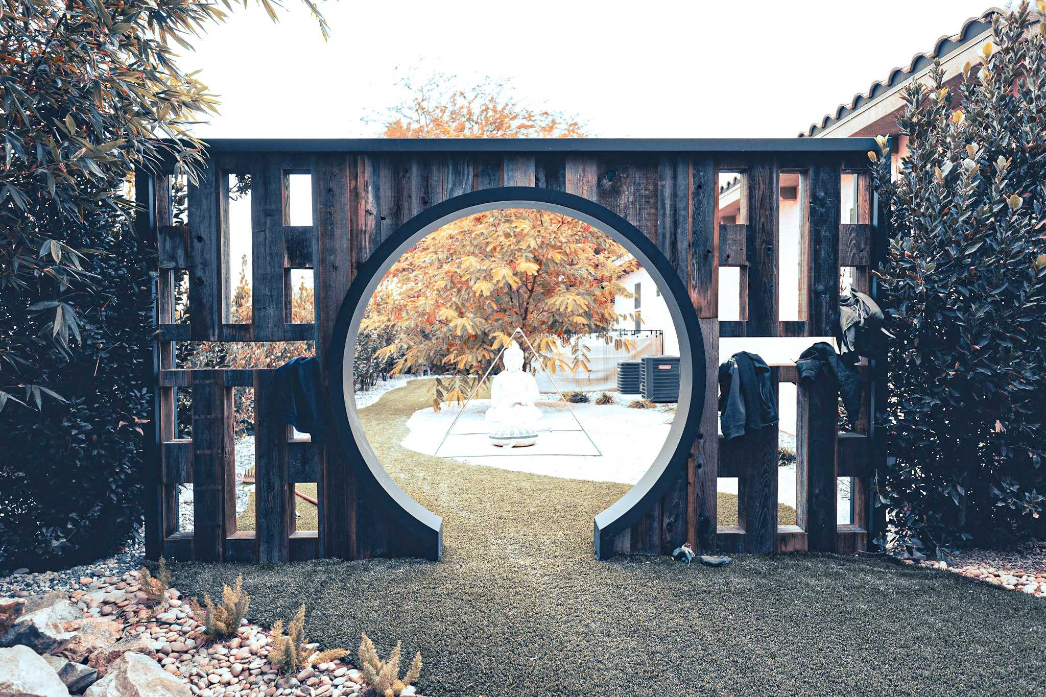 Dark wood moon gate with circular opening framing backyard view, flanked by evergreen plants